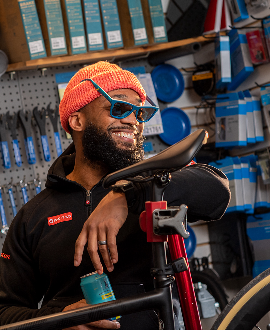 Cyclist holds can of Run Wild non-alcholic beer in bike shop advertising for Athletic Brewing Co.