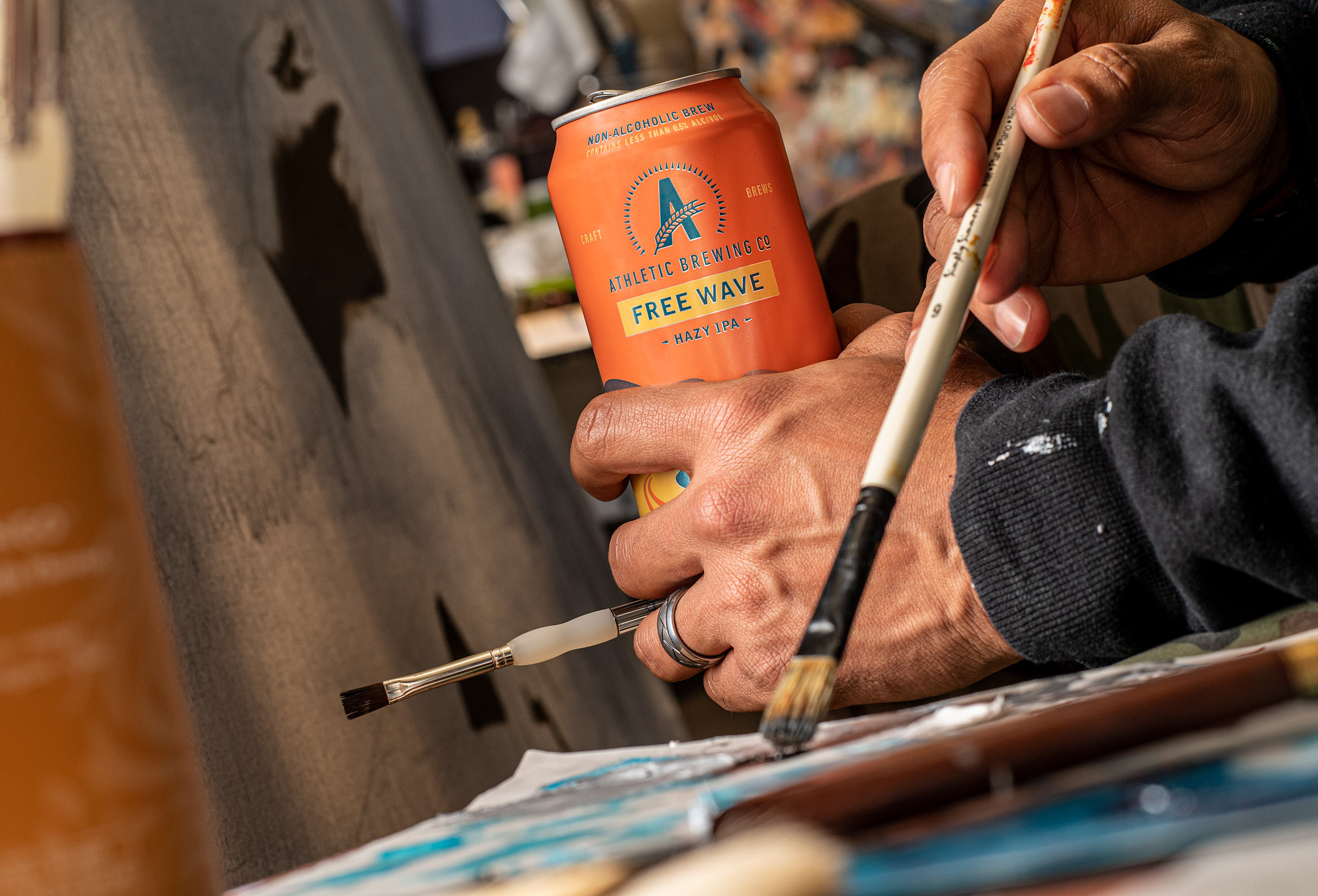 Close up of artist hands painting with can of Free Wave non-alcoholic beer - advertising for Athletic Brewing Co.