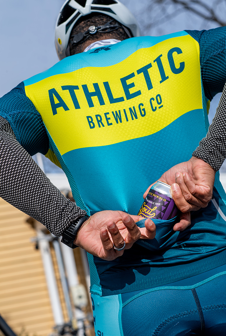 Cyclist puts can of Soul Sour into pocket of cycle kit - advertising for Athletic Brewing Co.