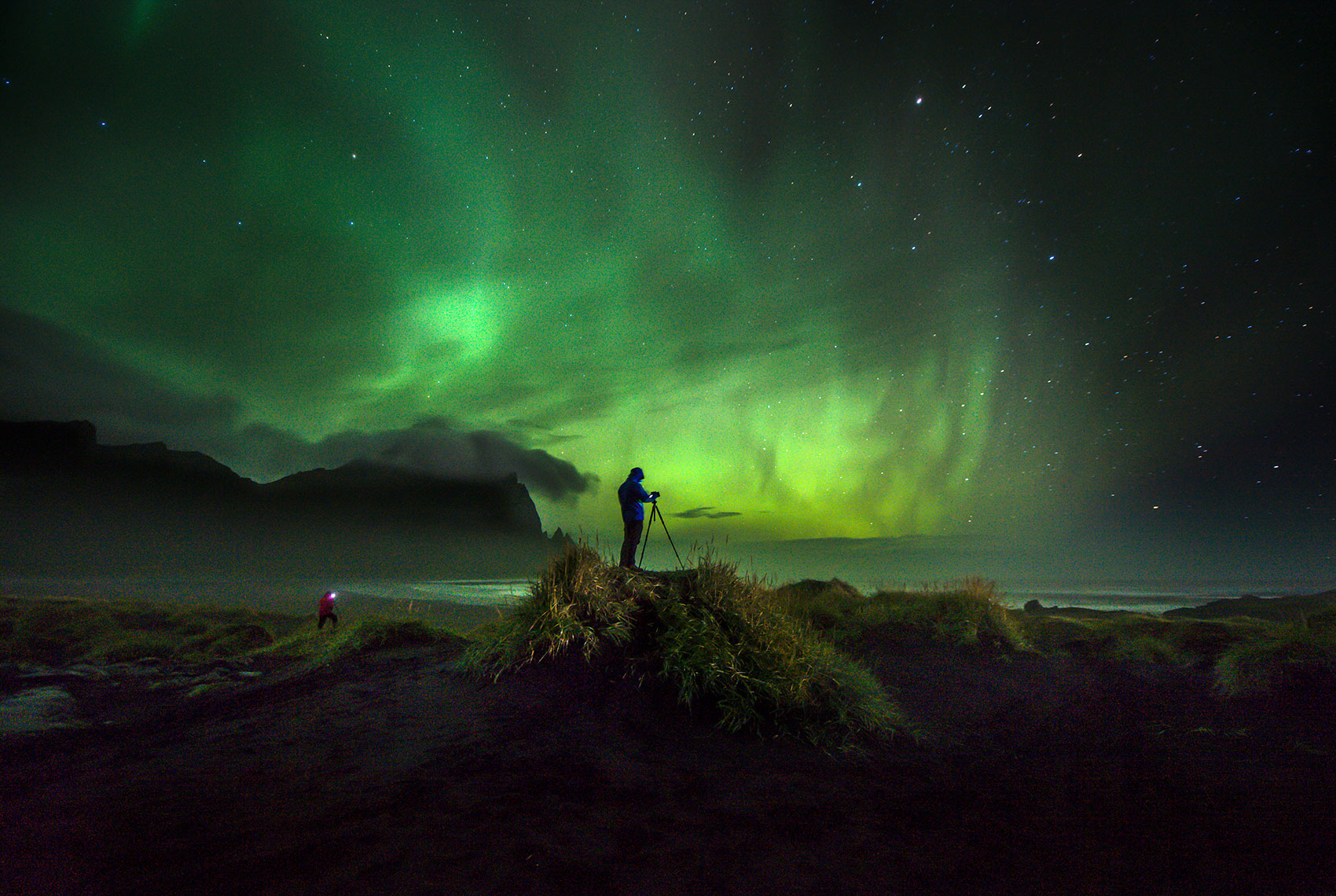 Photographer with camera on tripod photographs the northern lights in Iceland