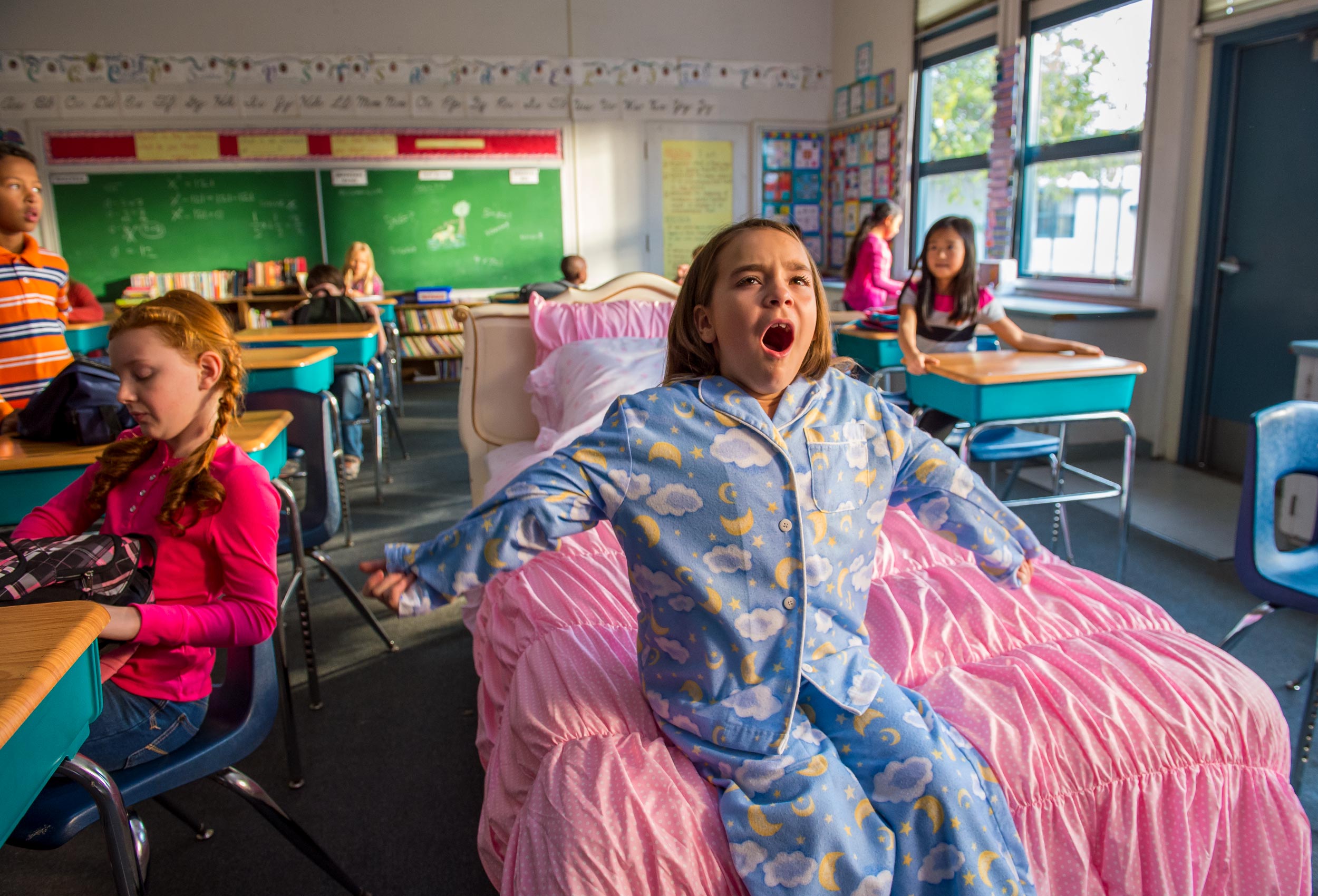 Young girl wearing pajamas sits on bed yawning in school room from Children