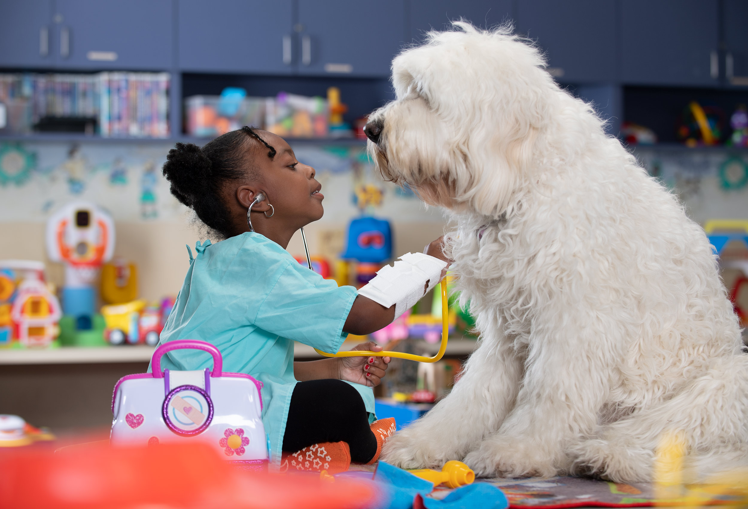 Little girl plays doctor with Goldendoodle therapy dog Wally B Doodle in pediatric playroom at Overlook Medical Center
