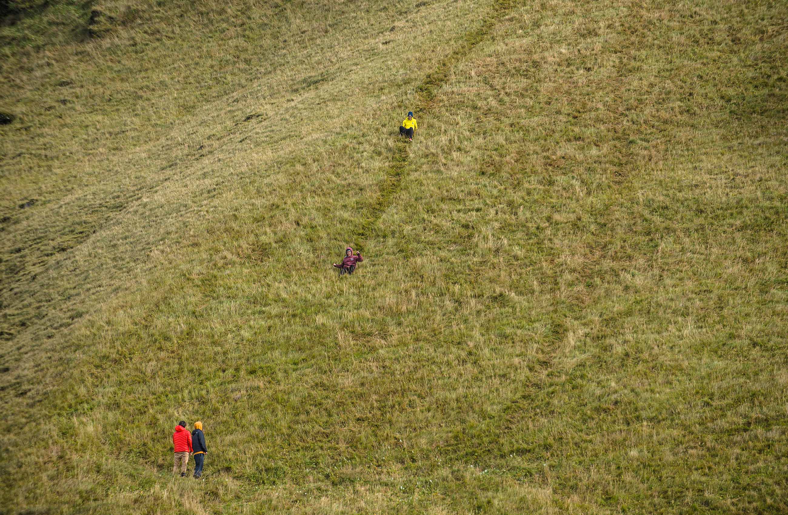 People slide down steep grass hill at Reynisfjara Iceland