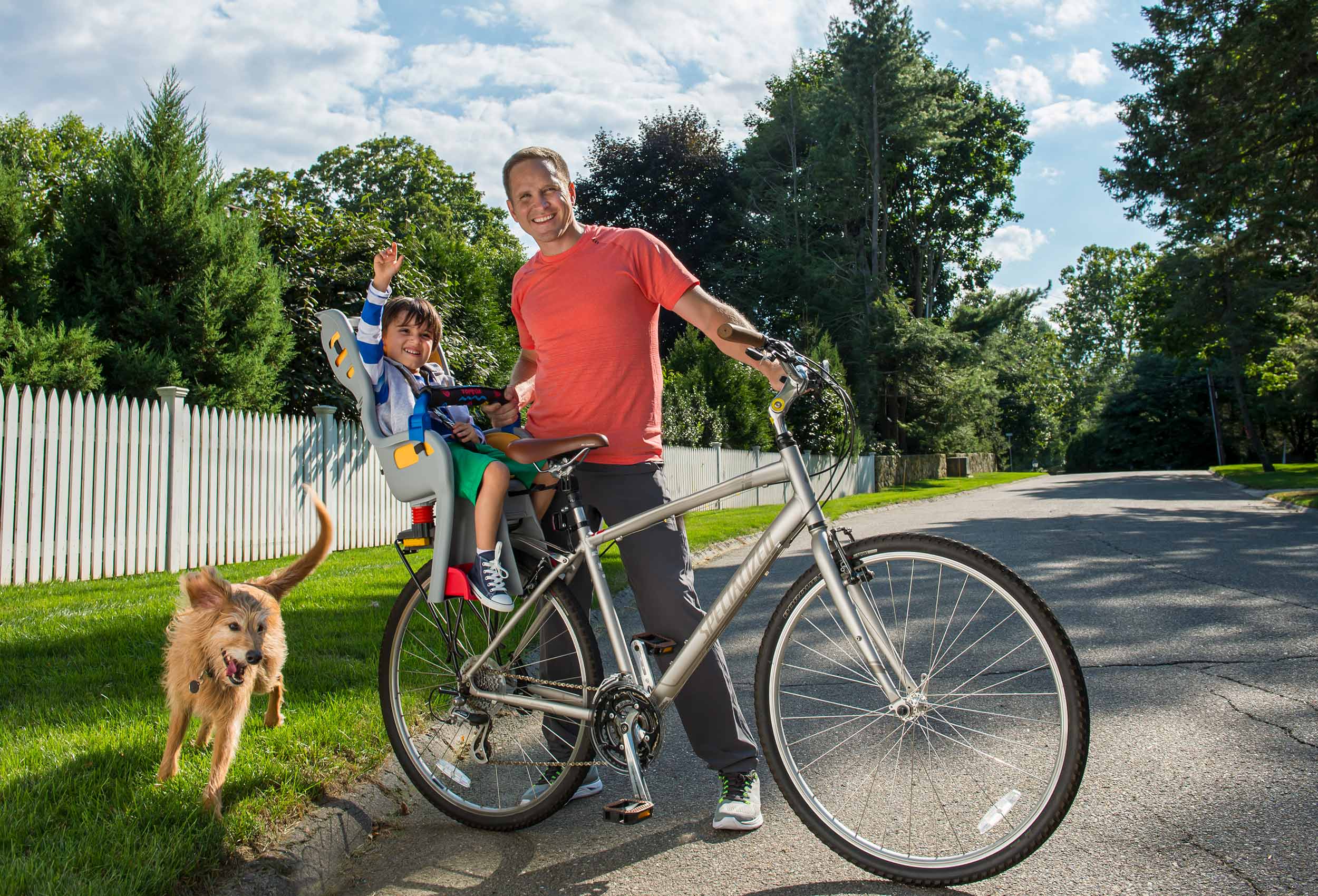 Father takes toddler on bike ride with dog on suburban street