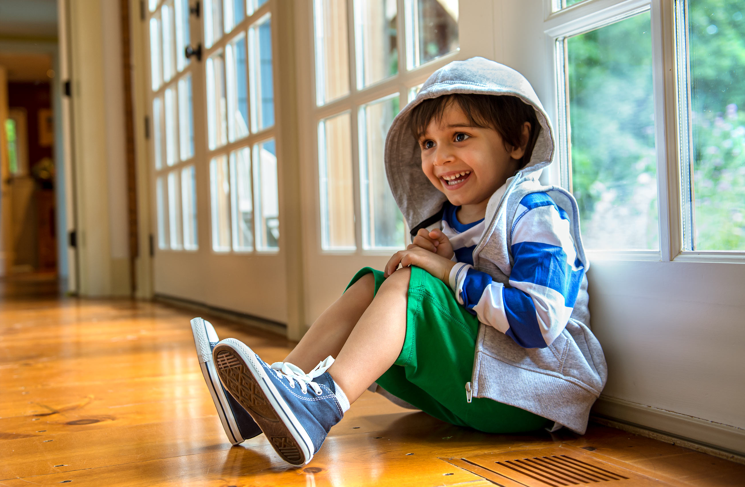Little boy sits on wood floor leaning against wall of window s