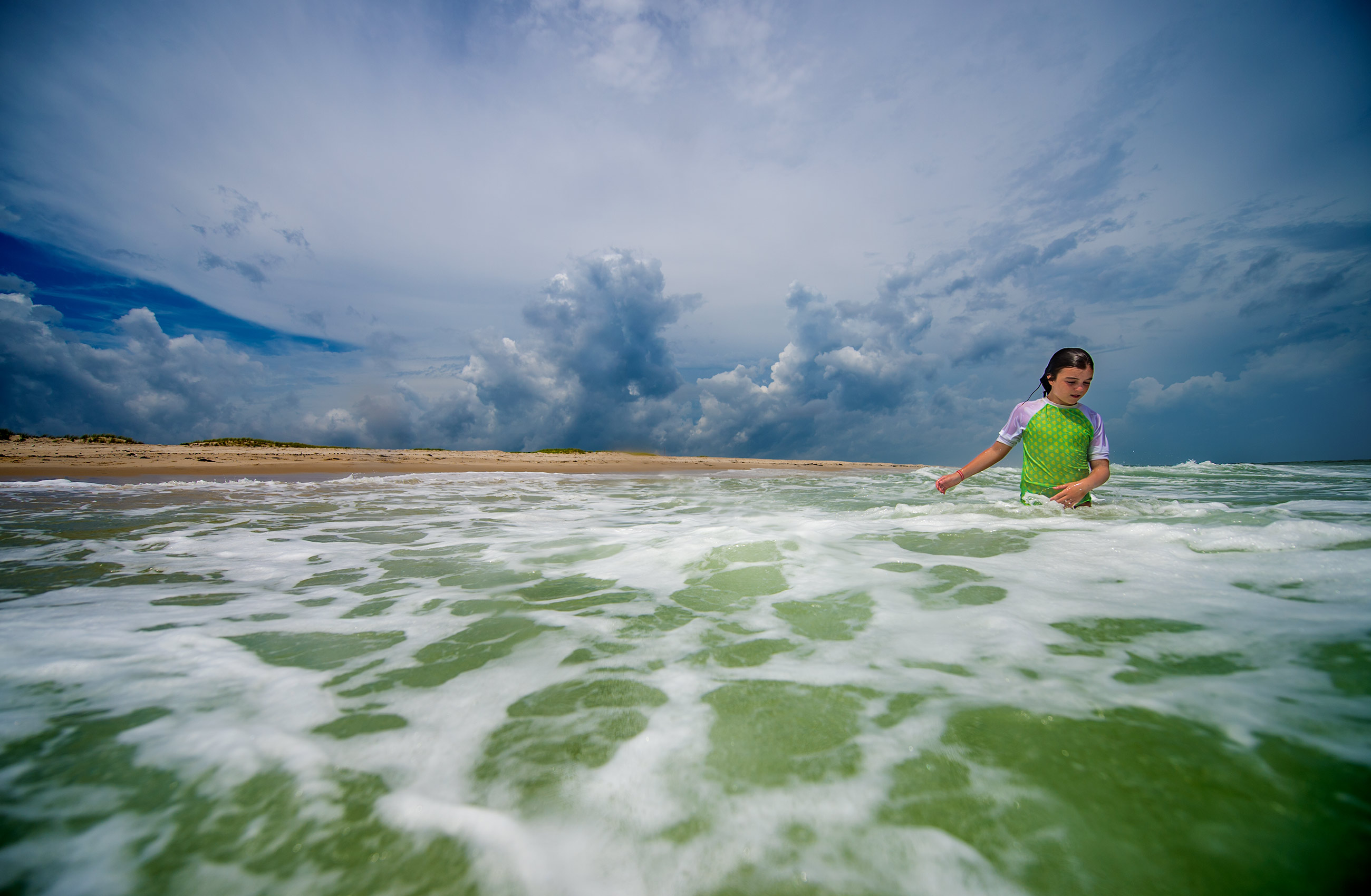Storm clouds over  girl in ocean at Island Beach State Park 