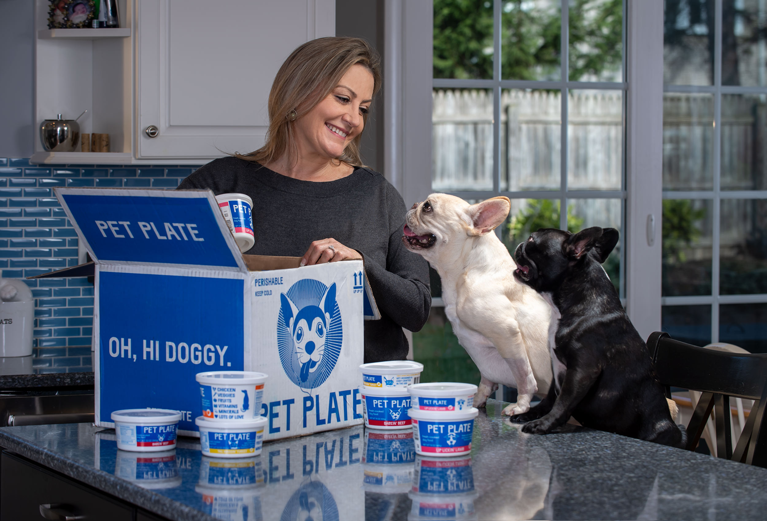 Dog mom opens box of Pet Plate  dog food delivery with two French Bulldogs