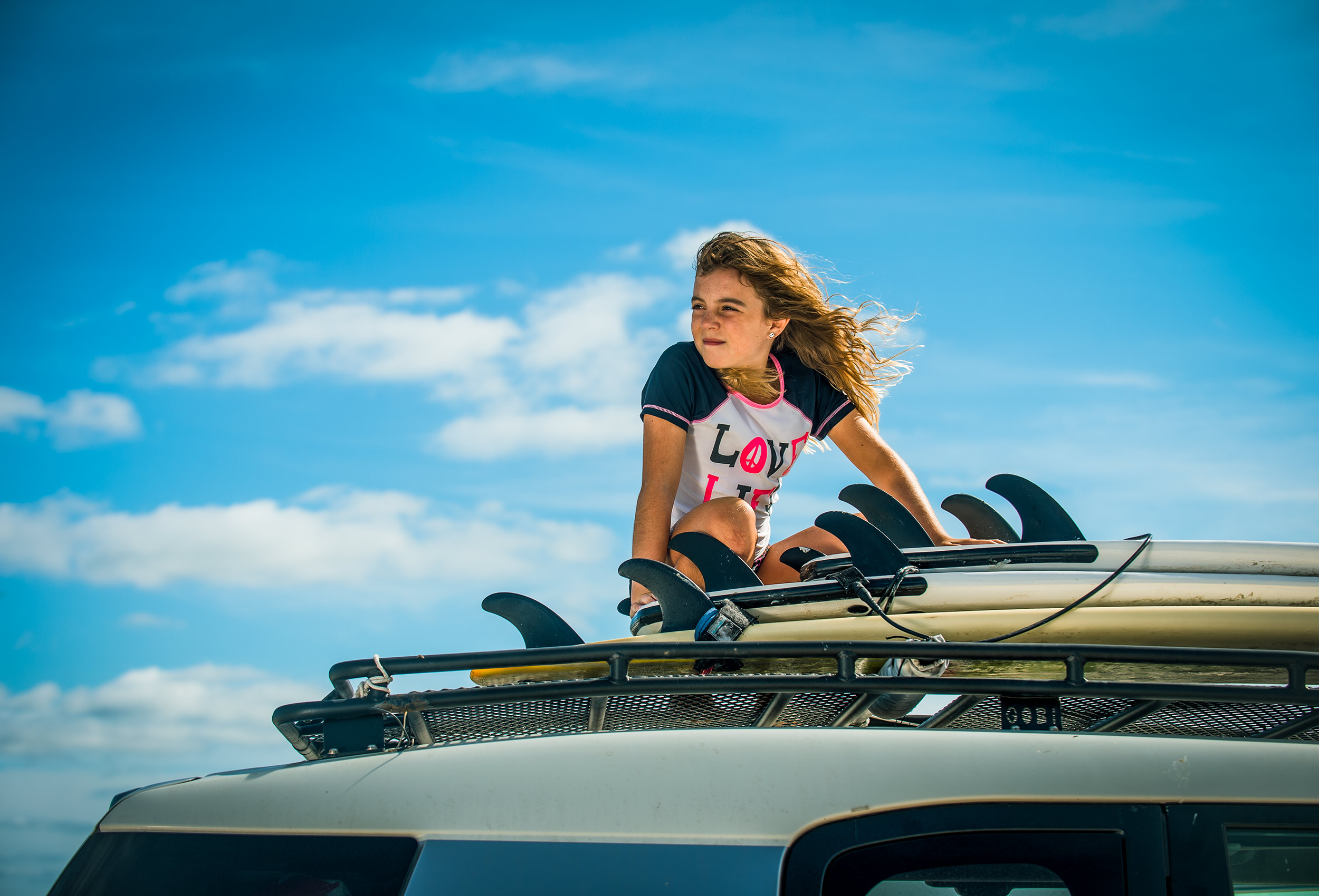 Teen girl with surfboards on roof of SUV blue sky