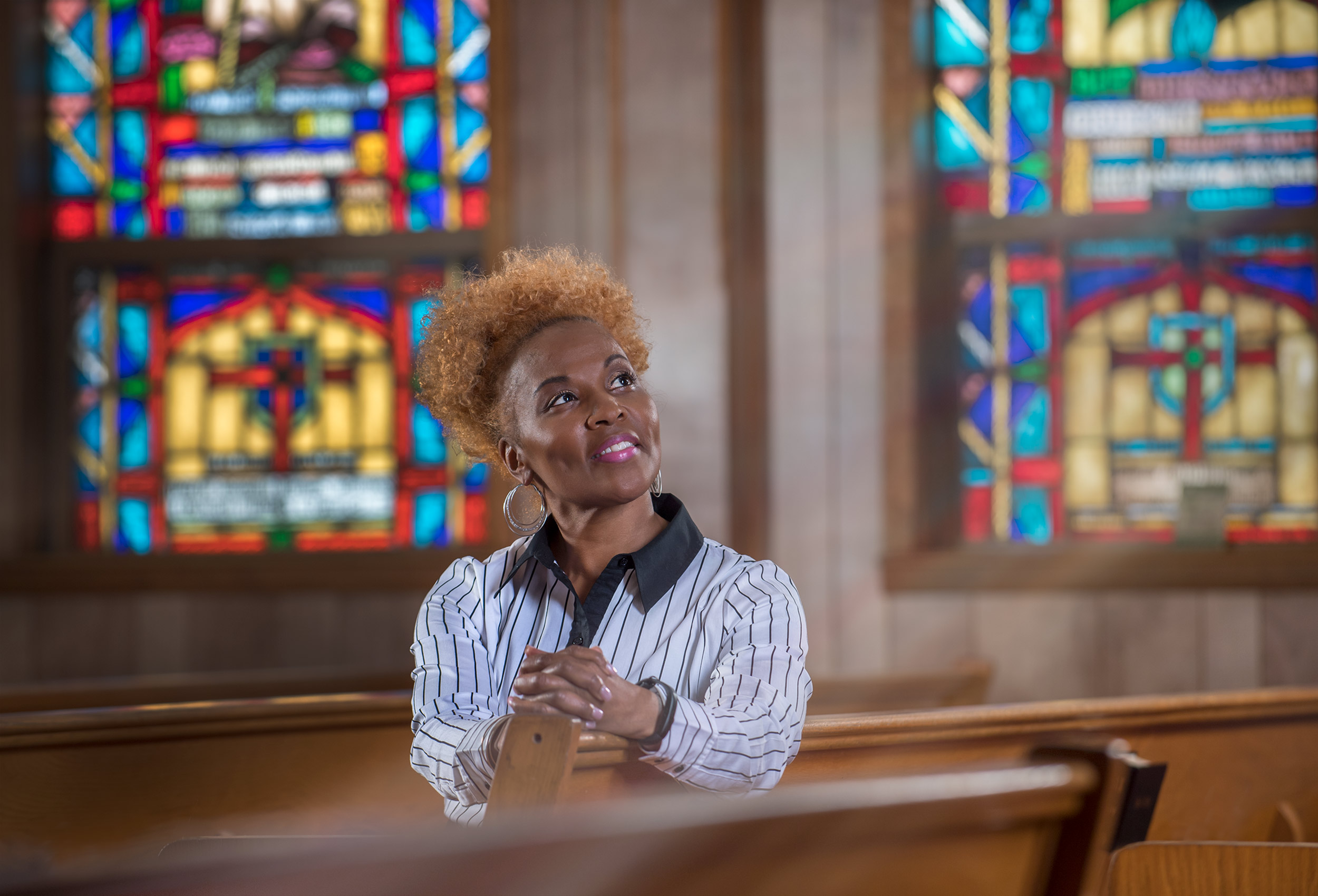 Prayerful woman sits in church pews with stained glass windows