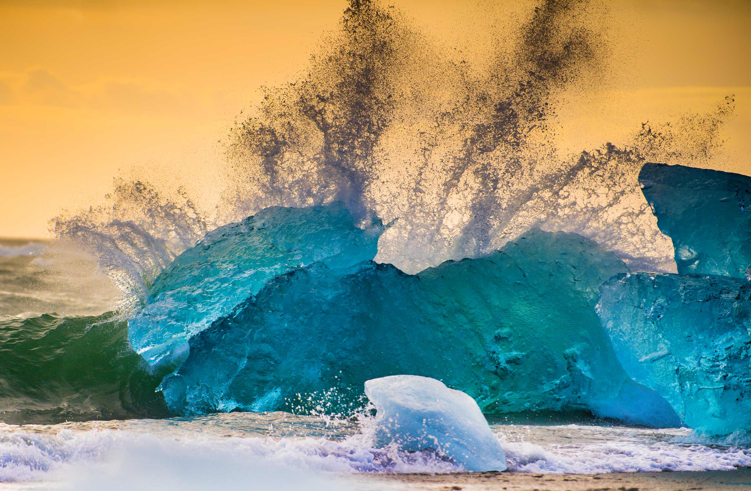 The sun rises backlighting  a blue iceberg at diamond beach Iceland