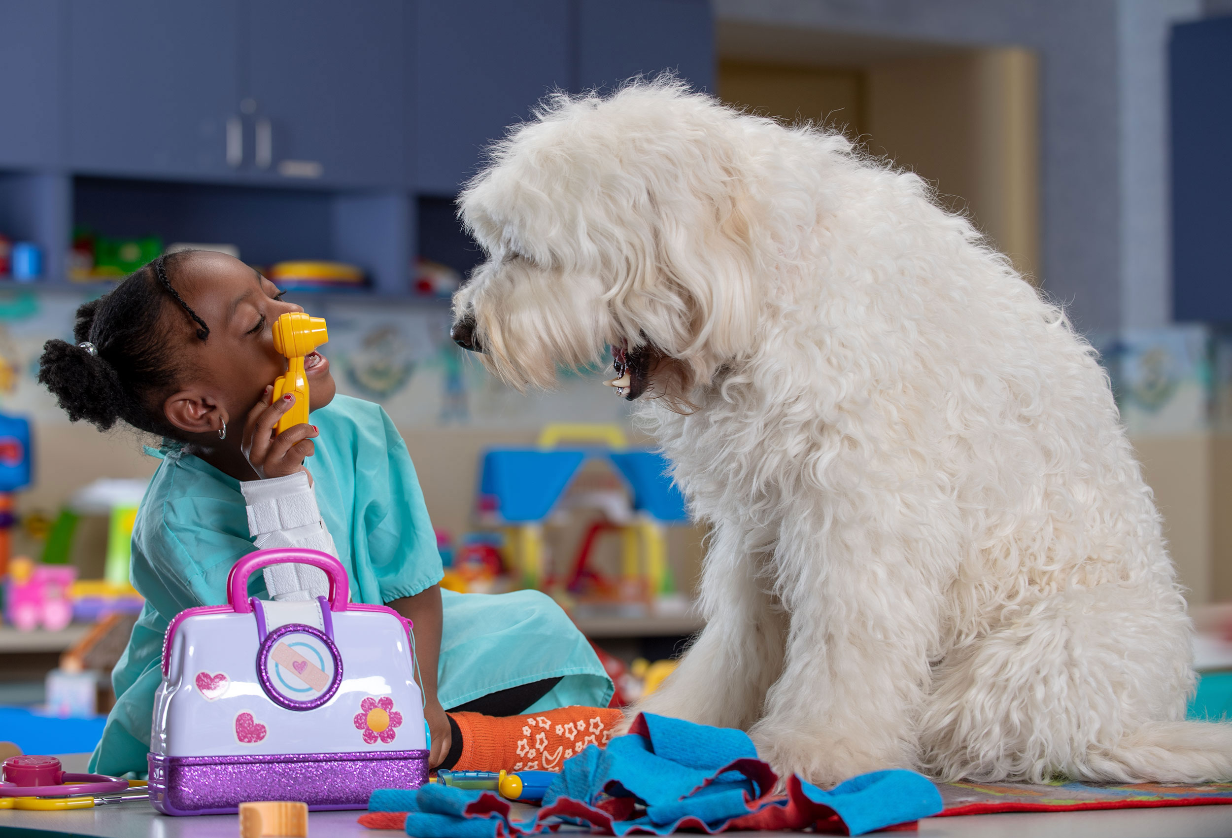 Little girl plays doctor with therapy dog Wally B Doodle  in pediatric playroom 