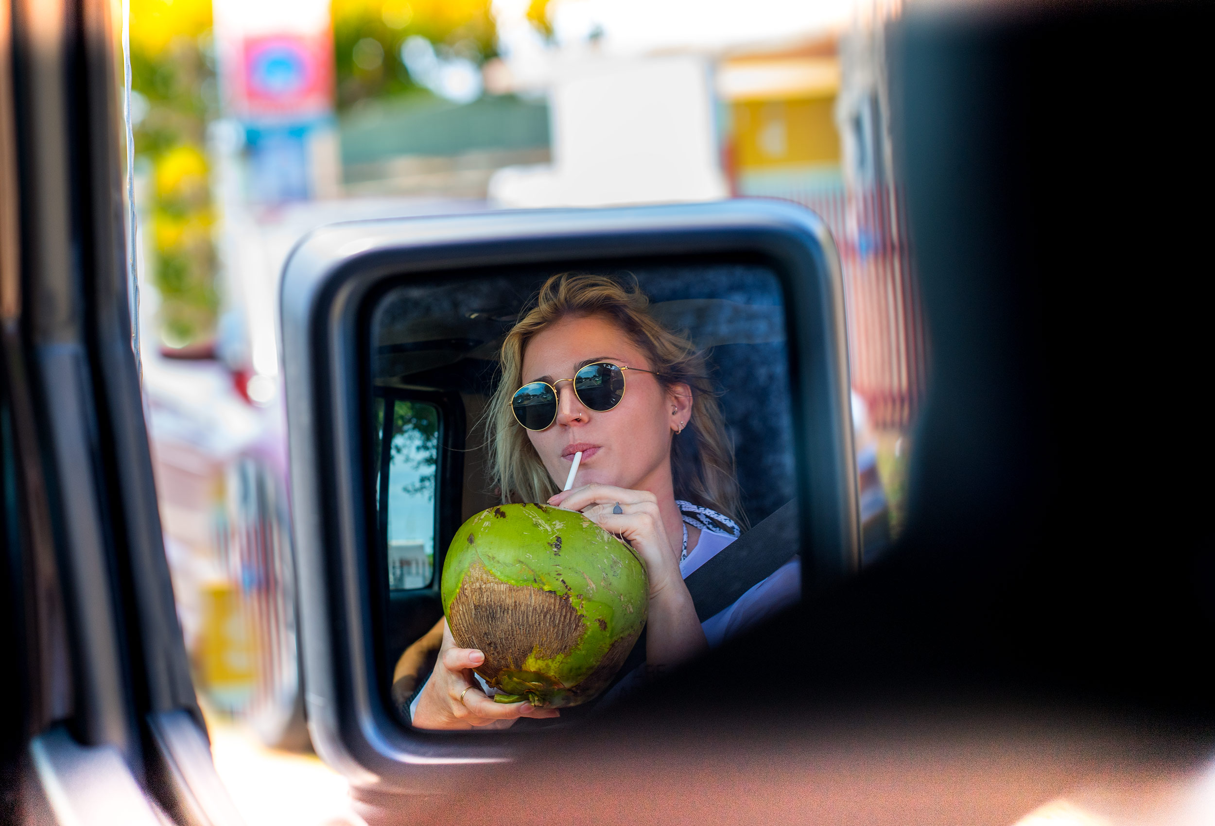Model holds coconut and drinks from straw in Jeep side mirror